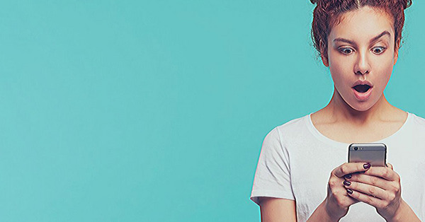 Fiatal lány ledöbbent arccal nézi az okostelefon kijelzőjét