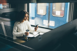 woman on train drinking coffee using mobile phone